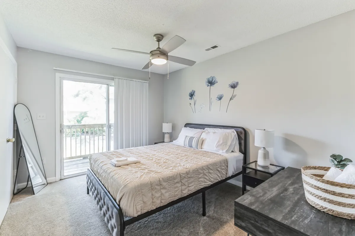 A calm bedroom scene with a comfortable bed, large window with blackout shades, decorative wall art, and nightstands. The layout and furnishings emphasize both comfort and practicality, with natural light hinting at the potential for a restful and private retreat.