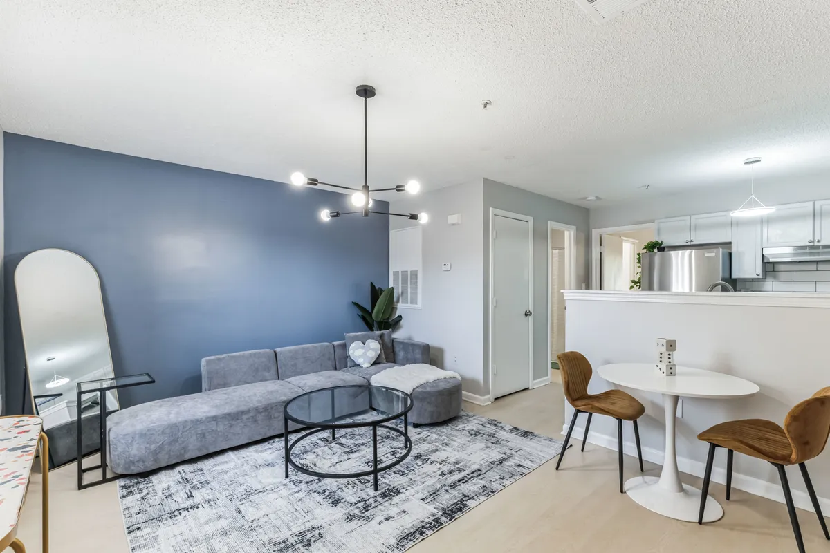 The image shows a contemporary and cozy living area with a comfortable sofa, a well-placed coffee table, a large mirror that enhances the sense of space, and partial views of the kitchen area. The layout suggests a social, inviting atmosphere ideal for relaxing or entertaining guests.