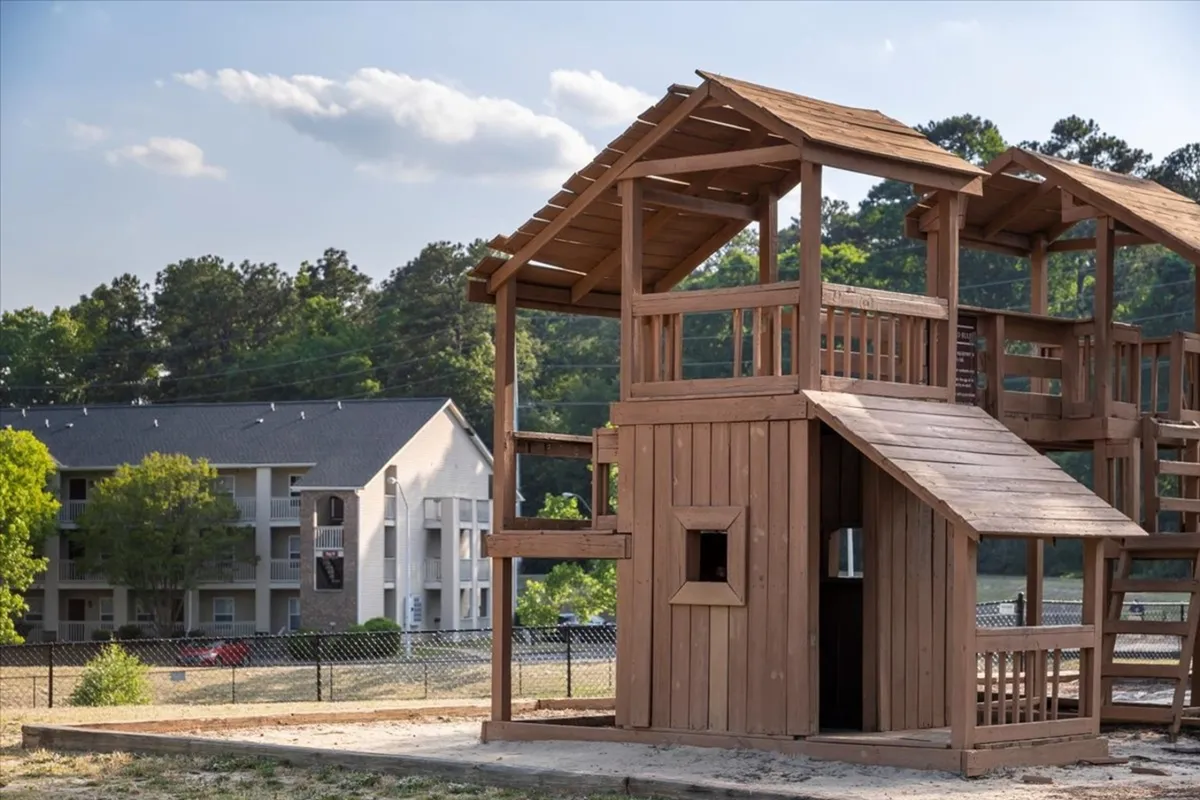 This image showcases a lively playground with colorful structures, surrounded by greenery and set against a backdrop of residential buildings. Children are playing, and families are gathered, illustrating a welcoming community environment.