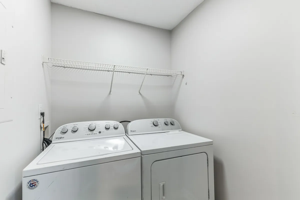 This image features a dedicated laundry area, with a washing machine and dryer side by side beneath a convenient storage shelf. The clean, organized setup emphasizes ease and efficiency for handling laundry in the comfort of your own home.