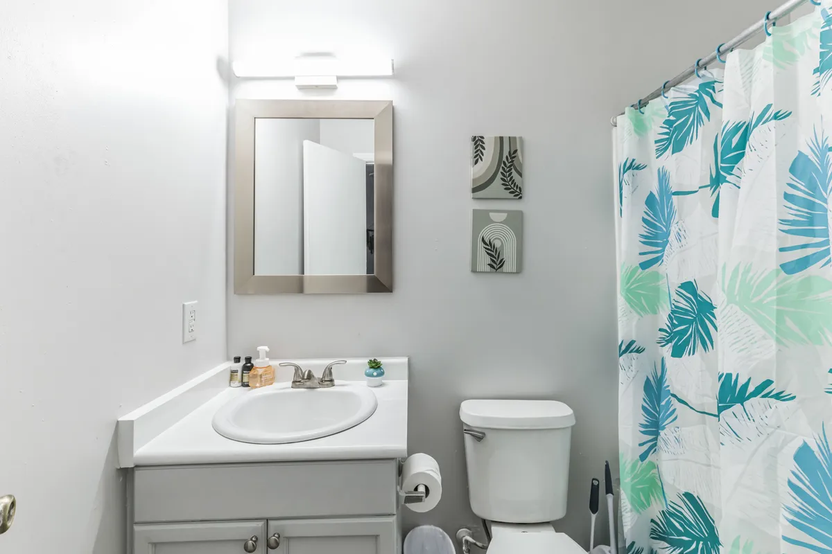 A bright, calming bathroom scene featuring a large mirror over the sink, fresh towels, a shower curtain, and tasteful wall art. The space appears clean and thoughtfully appointed, emphasizing relaxation and daily routines.