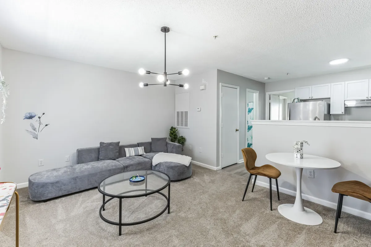 A spacious modern living area with a comfortable sofa, coffee table, stylish dining table, and an elegant chandelier. The space is filled with natural light and arranged to offer both relaxation and practical dining options.