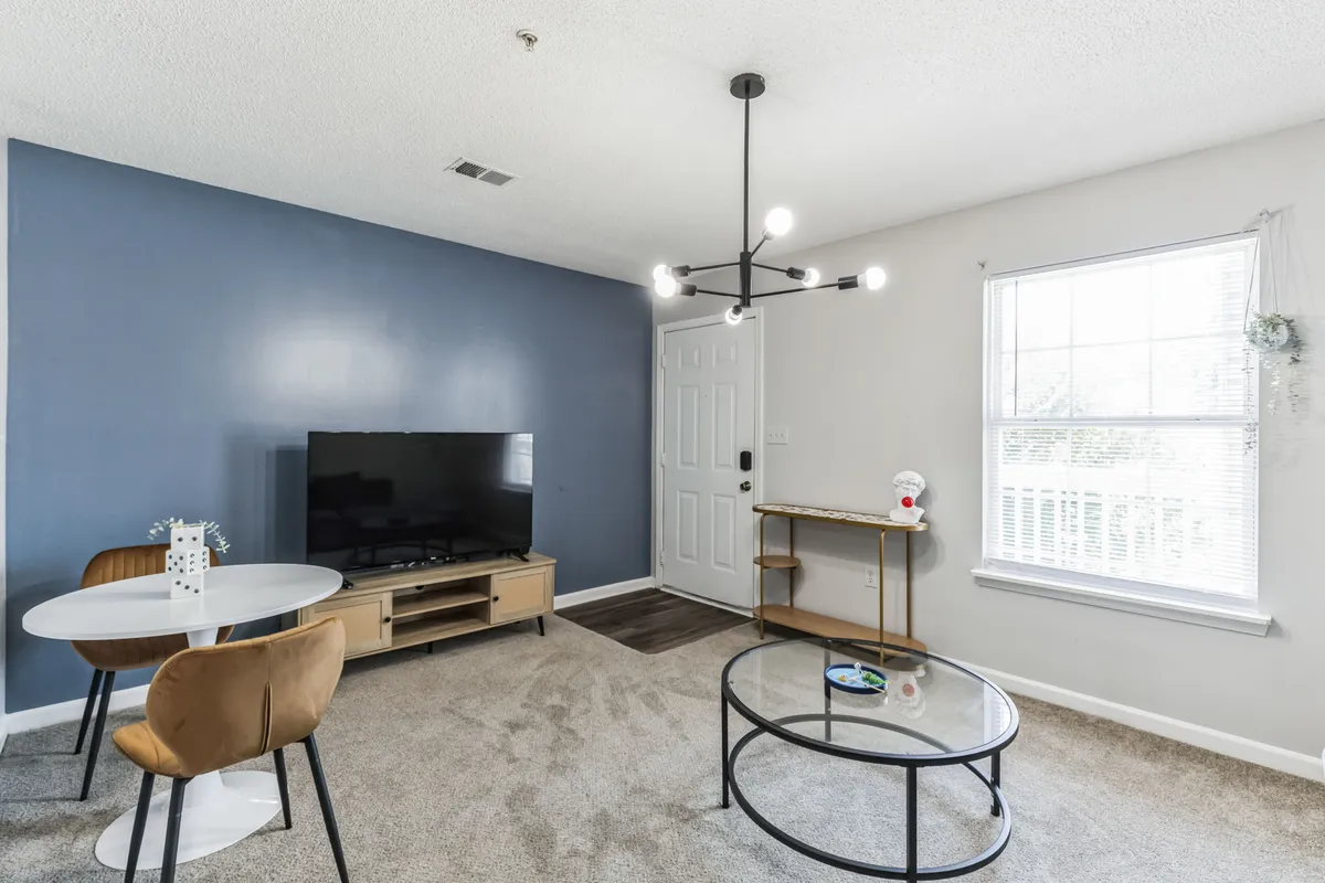 An inviting living and dining area with contemporary furnishings, a television, a table with chairs, and a prominent entry door, reflecting a seamless blend of comfort and style. The lighting and layout evoke a sense of homecoming after a day out.